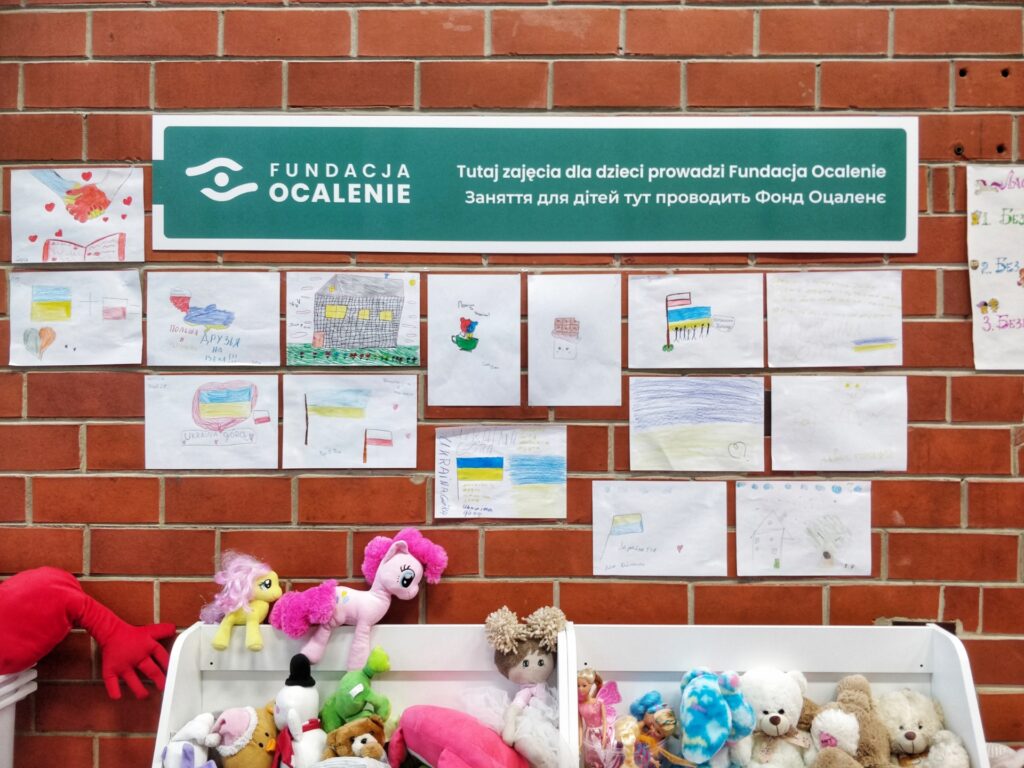 Fundacja Ocalenie sign in a refugee daycare centre with children's drawings underneath it